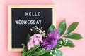 Hello Wednesday text on black letter board and bouquet colorful flowers on pink background. Concept Happy Wednesday. Template for