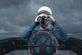 Helmsman with binoculars and cap viewing the coast and light tower