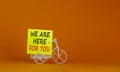 Help is here symbol. Wooden clothespin with yellow paper. Words `we are here for you`. Miniature bicycle model. Beautiful orange Royalty Free Stock Photo