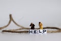 A HELP text alphabet cube in a rope. Miniature people.