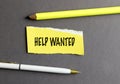 Help wanted message on torn yellow paper with pencil and pen on dark gray background Royalty Free Stock Photo