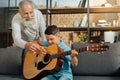 Happy grandfather giving grandson tips on playing guitar Royalty Free Stock Photo