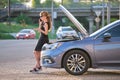 Helpless woman standing near her car with open bonnet calling road service for help. Young female driver having trouble Royalty Free Stock Photo