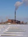 A wintery scene of an urban powerplant with frozen lake in the foreground