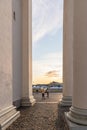 Narrow vertical view of people between tall columns and sunset sky.