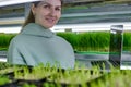 Between helves with lot wheat microgreens girl poses for camera with laptop Royalty Free Stock Photo