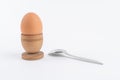 Hen egg in old wooden egg stand with metal spoon, isolated on white background. Breakfast minimalistic concept. Food conceptual Royalty Free Stock Photo