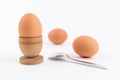 Hen egg in old wooden egg stand with two more eggs and metal spoon, isolated on white background. Breakfast minimalistic concept. Royalty Free Stock Photo