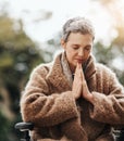 Her beliefs give her the strength to carry on. a senior woman holding her hands together in prayer while sitting in her