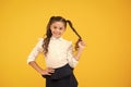 Her twisted hairdo. Small girl winding long hairdo around her finger on yellow background. Little kid with ponytail