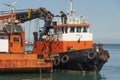 Greek tugboat and crew alongside a crane barge to move the vessel out of port.