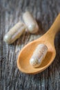 Herb capsules spilling in wooden spoon.