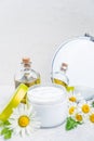 Herbal cosmetic body cream in opened container, natural oil, fresh chamomile flowers, mirror on a white background