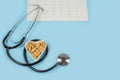 Herbal pills in heart shaped wooden plate, stethoscope and cardiogram on blue background.