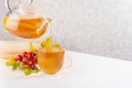 Herbal rose hips tea in teapot pouring into cup, autumn rose hip leaves and berry on white wood table with copy space. Royalty Free Stock Photo