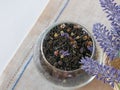 Herbal tea with blue dried flowers in a round glass vase on a canvas napkin, lavender flowers