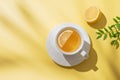 Herbal tea with lemon in a white cup on a yellow background with shadows