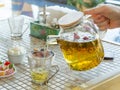 Herbal tea is poured from a transparent teapot into a glass cup on a cafe table