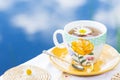 Herbal tea in teacup decorated with flowers outdoors in background of blue sky with clouds