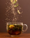 Herbal vitamin tea. Ingredients falling into glass cup with drink. Close up shot in motion on brown background. Side Royalty Free Stock Photo