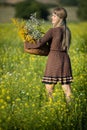 A young herbalist with a basket of herbs walks through a field full of flowering rapeseed. Goldenrod and wintercress.