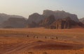 a herd of camels walking across a desert next to mountains
