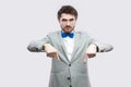 Here and right now. Portrait of serious bossy handsome bearded man in casual grey suit and blue bow tie standing pointing and