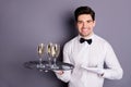 Here your order. Positive cheerful waiter bring client guest alcohol wine standing on tray show point hand wear white