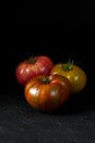 Hereditary tomatoes. Three tomatoes of different colors on a black textured background close-up