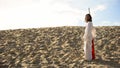 Hermit with staff walking in desert looking to camera, asceticism and fasting