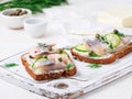 Herring smorrebrod - traditional Danish sandwiches. Black rye bread with herring on white wooden board, side view