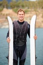 Hes an avid skier. Smiling water-skier holding his skis alongside the lake.
