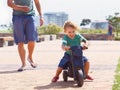 Hes born to be a biker boy. A happy toddler boy riding is toy motorbike outside while his father runs after him from