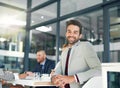 Hes a confident go getter. Portrait of a businessman sitting in an office with his colleagues in the background.