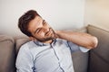 Hes feeling a bit of tension on his neck. Shot of a handsome young man holding his neck in pain while relaxing on a sofa Royalty Free Stock Photo