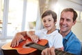 Hes going to be a great guitarist. a father and his young son sitting together in the living room at home playing guitar Royalty Free Stock Photo