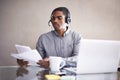 Hes got access to all the client files. A young businessman wearing a headset going through some paperwork at his laptop