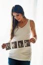 Hes got his mothers good looks already. a happy pregnant woman holding up a series of ultrasound pictures in front of a