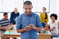 Hes got the latest news at his fingertips. Young businessman texting on his phone with colleagues working behind him. Royalty Free Stock Photo