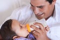 Hes a hands-on dad. A father feeding his baby boy a bottle of milk while seated on the couch. Royalty Free Stock Photo