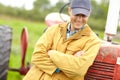 Hes happy with his farm. a smiling farmer standing next to his tractor with his arms crossed and looking down. Royalty Free Stock Photo