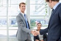 Hes just been promoted. two businessmen shaking hands in an office setting.