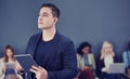 Hes always looking toward the future. a handsome young businessman using a tablet with his colleagues in the background. Royalty Free Stock Photo