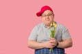 Hesitating plump man waiting for girlfriend with flowers on pink background