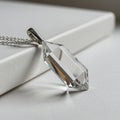 A hexagonal, clear crystal pendant with precise facets is attached to a delicate silver Royalty Free Stock Photo