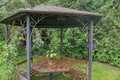 Hexagonal ornate gazebo with wooden benches, table in middle, with vase of white flowers and gray wicker baskets with flowers