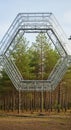 A hexagonal steel structure stands suspended in a forest setting with tall pine trees Royalty Free Stock Photo