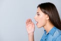 Hey, listen here! Close up side-view portrait of attractive woman telling news, shouting and holding hand near her open mouth, st