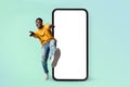 Hey you, check this website. Excited black man standing near huge smartphone with blank screen, mock up Royalty Free Stock Photo