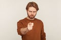 Hey you! Portrait of angry bossy strict man with beard wearing sweatshirt pointing finger, indicating direction